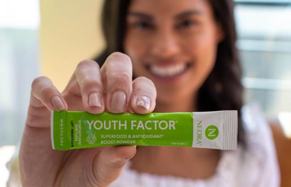 A woman holding up a packet of Youth Factor® Superfood & Antioxidant Boost Powder.
